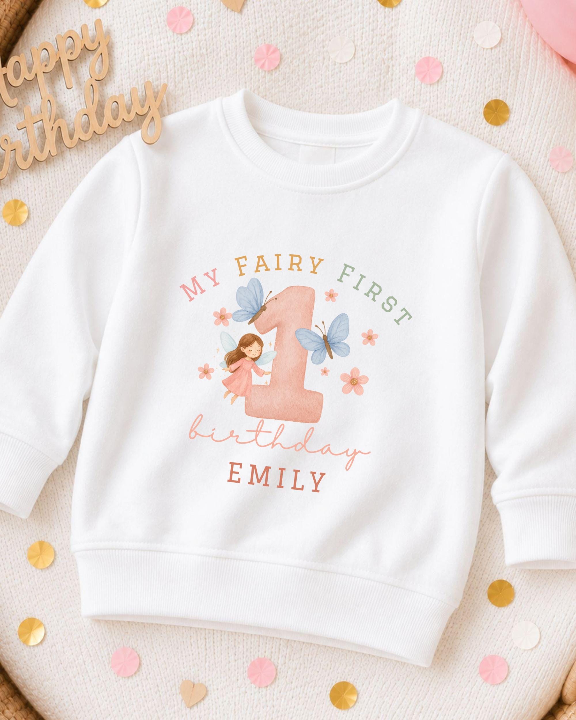 A white sweatshirt with a personalized design for a first birthday, featuring a fairy and the number 1.