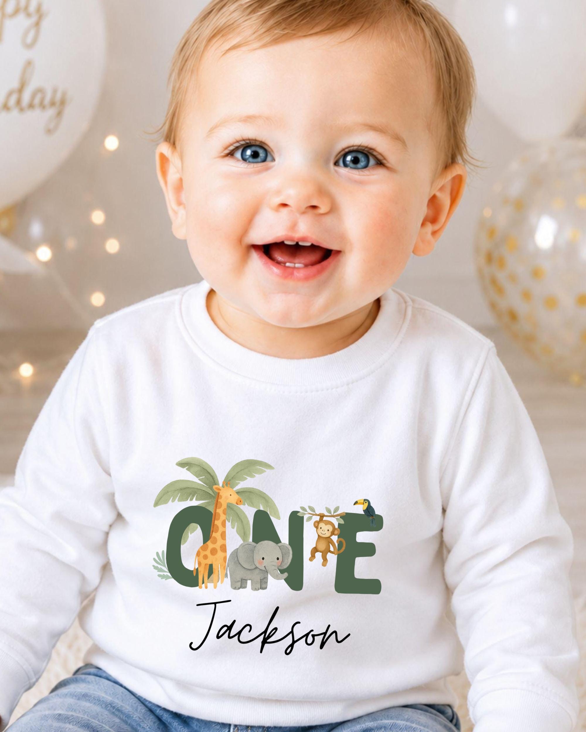 A smiling baby boy wearing a white shirt with a jungle-themed graphic and the name "Jackson" printed on it.