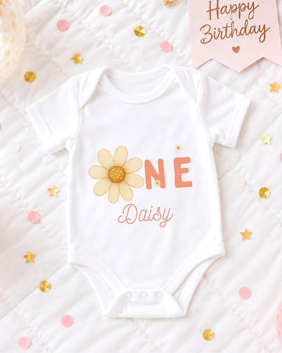 A white bodysuit with a flower design and the text "Daisy" printed on it, surrounded by confetti and a birthday card.