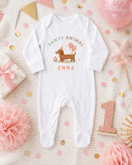 A white onesie with a dog and balloons, surrounded by birthday decorations and a pink balloon, with the text "Pawty animal Emma" on the onesie.