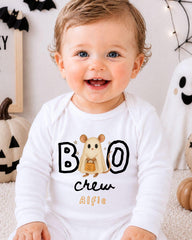 A smiling baby wearing a white onesie with a cartoon character and the text "BOO crew Alfie" printed on it.