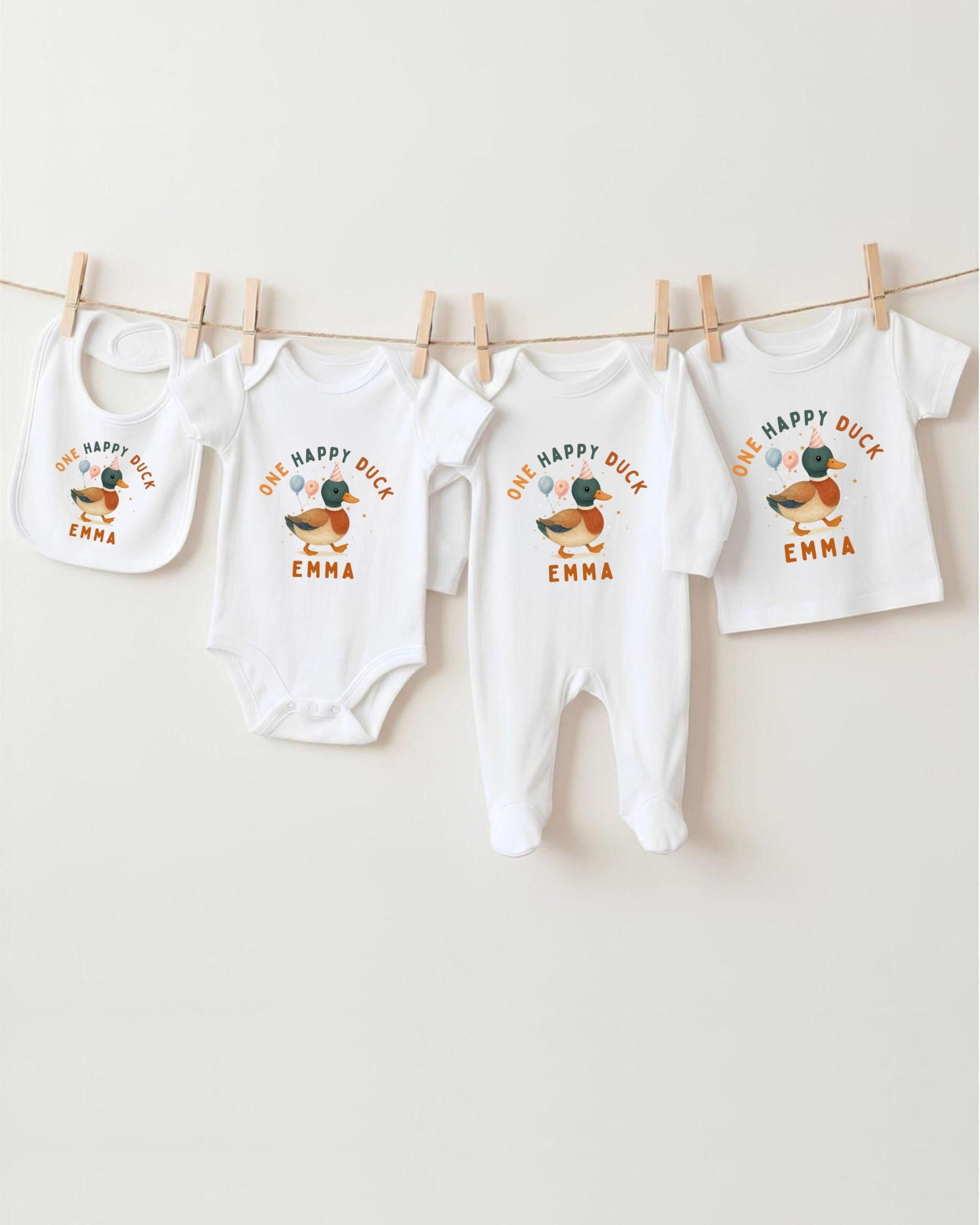 A row of four white baby clothes with a happy duck design, hanging on a clothesline.