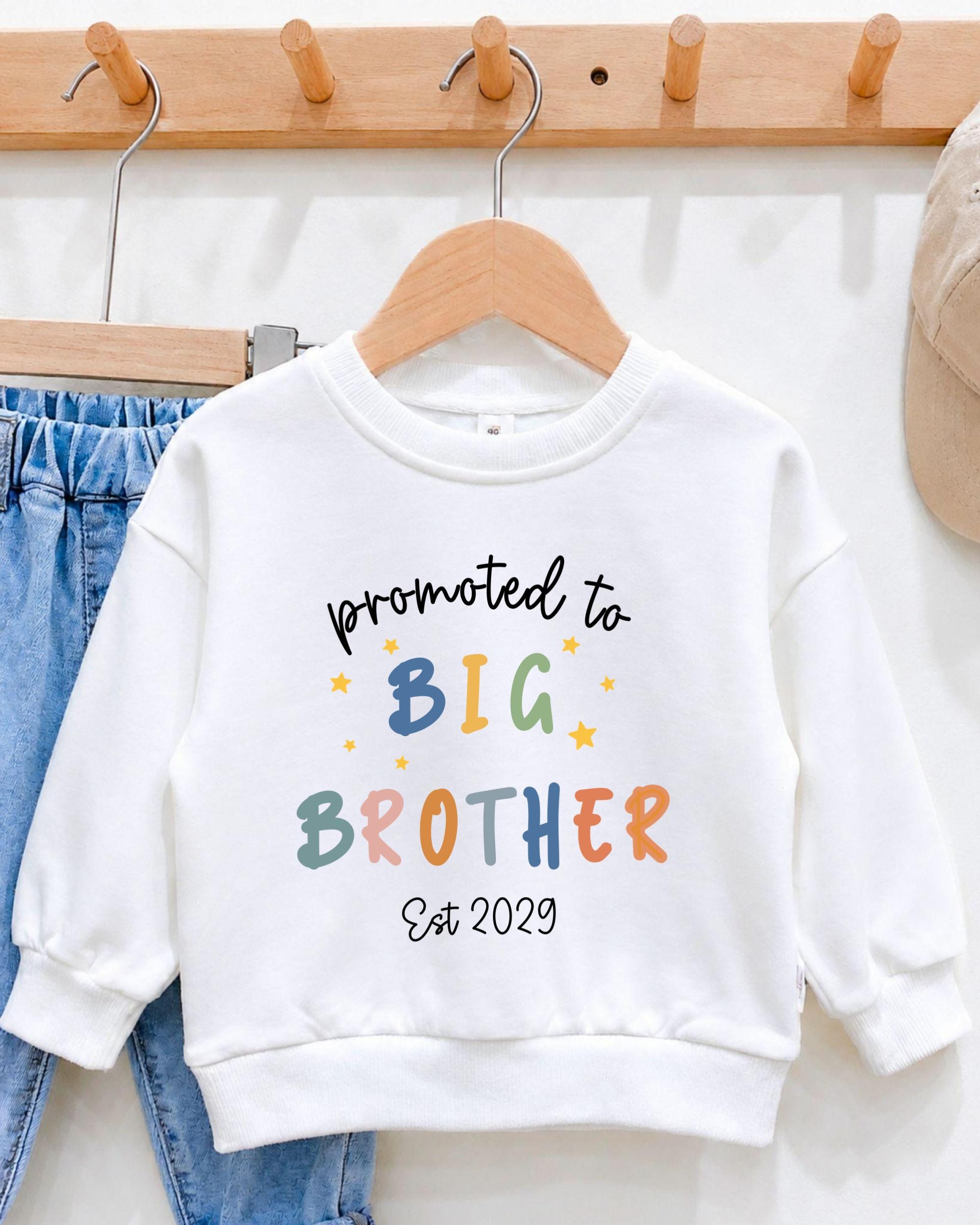 A white sweatshirt with text printed on it, hanging on a wooden hanger.