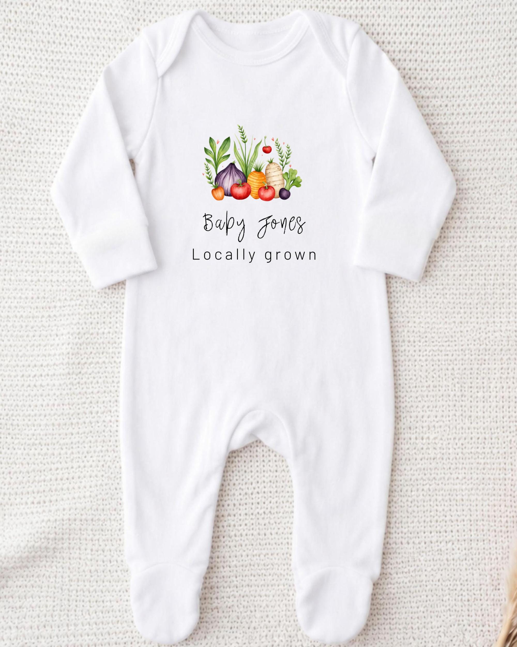 A white onesie with a graphic design of vegetables and the text "Baby Jones Locally Grown" printed on it.