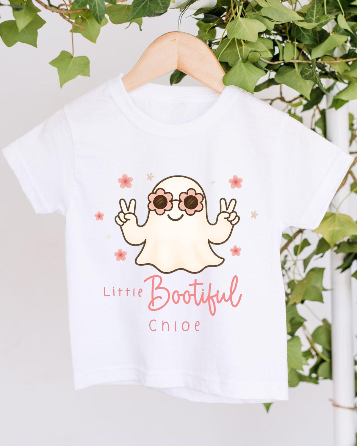 A white t-shirt with a cartoon ghost wearing sunglasses and holding a peace sign, with the text "Little Bootful Chloe" printed on it.
