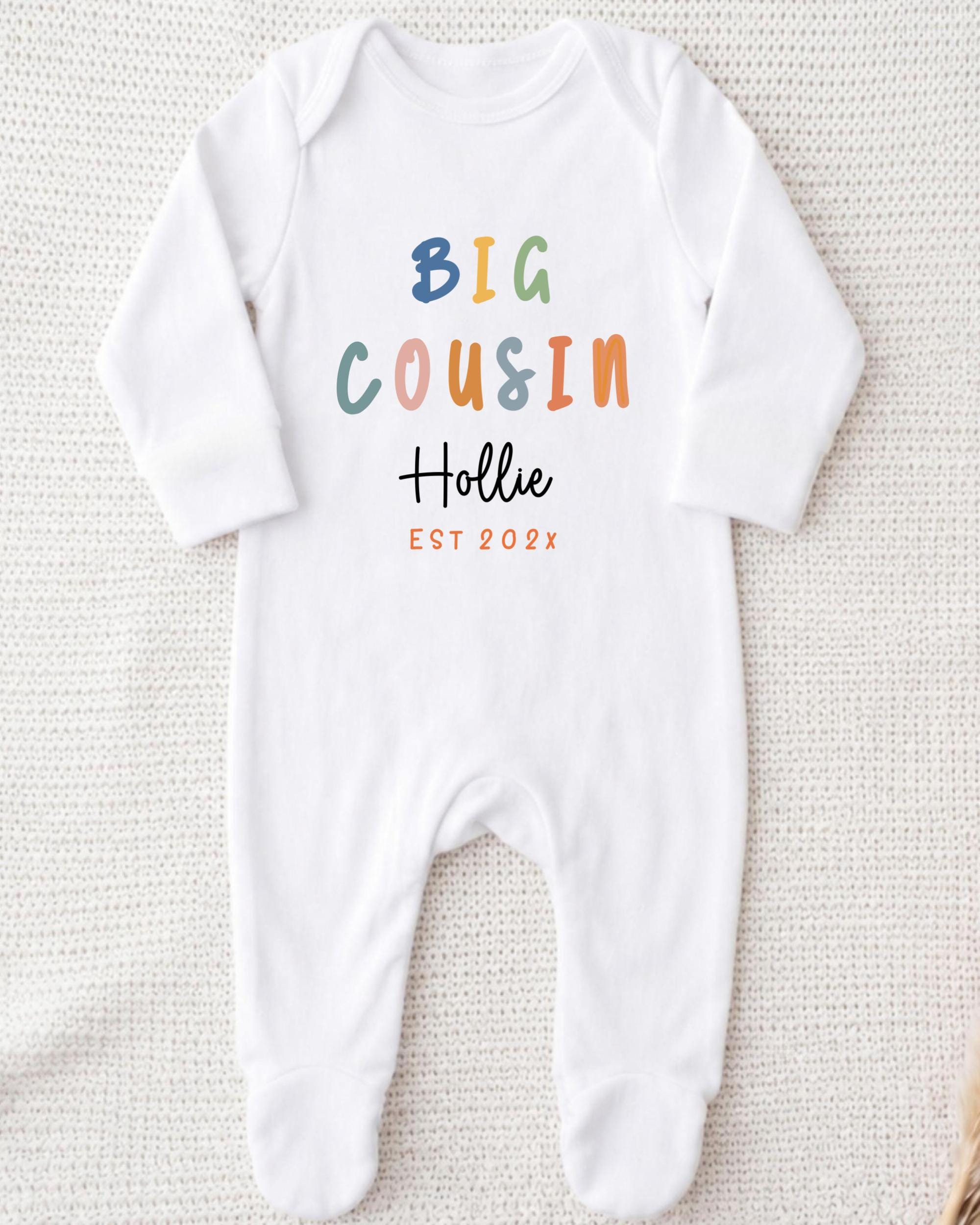 A white onesie with the text "BIG COUSIN Hollie EST 202x" printed on it.