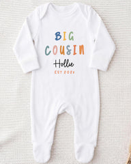 A white onesie with the text "BIG COUSIN Hollie EST 202x" printed on it.