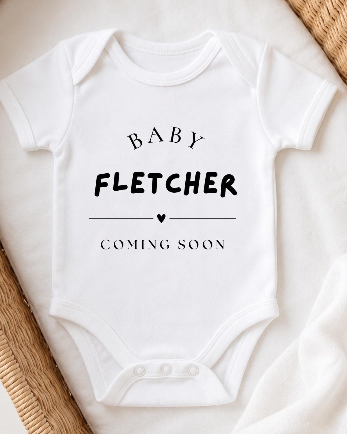 A white baby onesie with the text "BABY FLETCHER COMING SOON" printed on it.