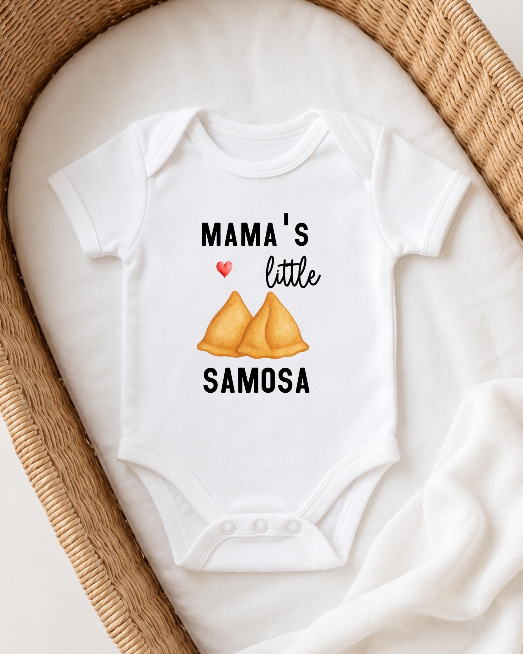 A white onesie with a printed design on it, featuring a heart symbol and the text "MAMA'S LITTLE SAMOSA".