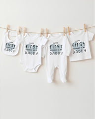 A row of white baby clothes with the text "Happy first birthday as my Daddy" printed on them, hanging on a clothesline.