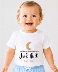 A smiling baby wearing a white t-shirt with a moon and crescent design and text that says "Love you to the moon & back Jack Mill Smith".