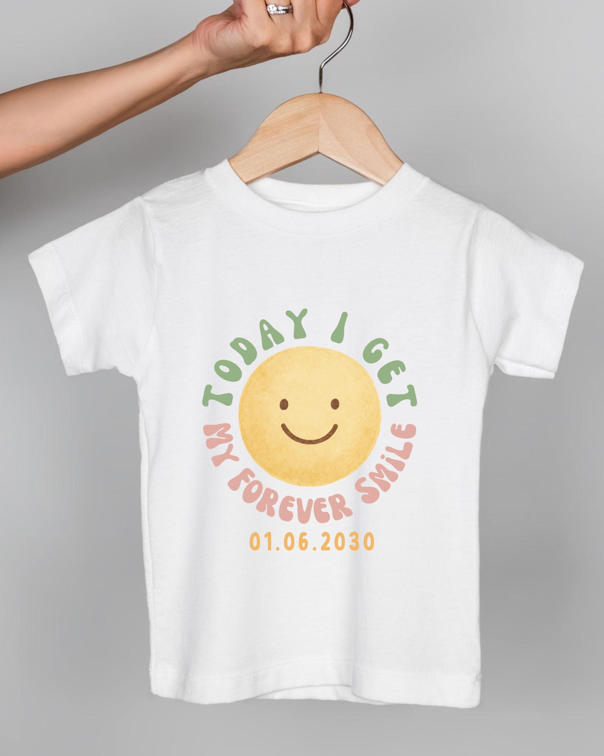 A white t-shirt with a cheerful smiley face design and text printed on it.