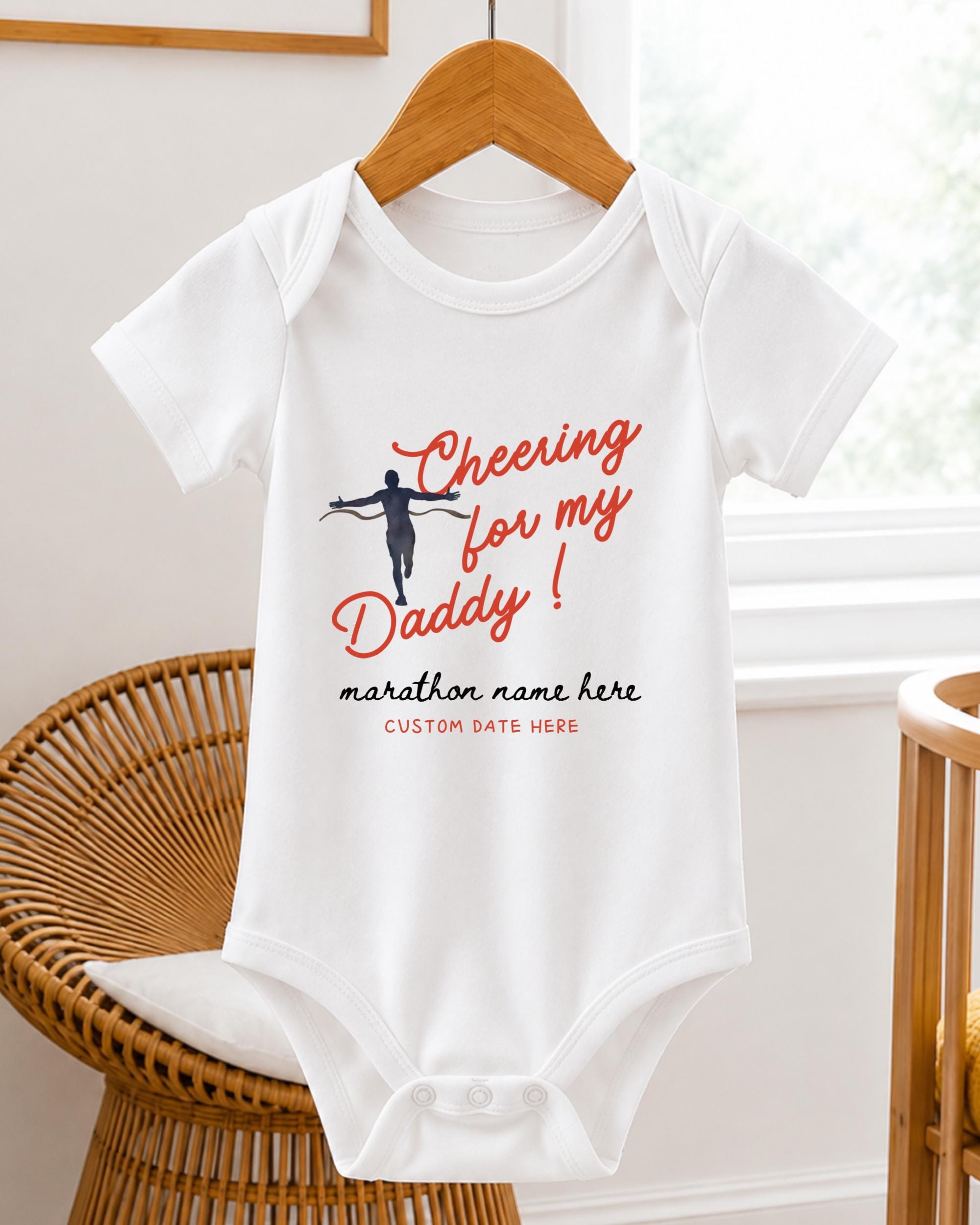 A white baby onesie with a graphic design and text printed on it, hanging on a wooden hanger.