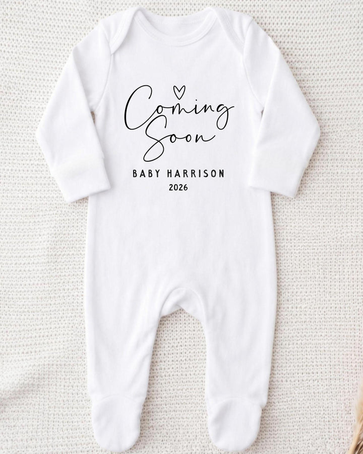 A white bodysuit with the text "Coming Soon" and "Baby Harrison 2026" printed on it.
