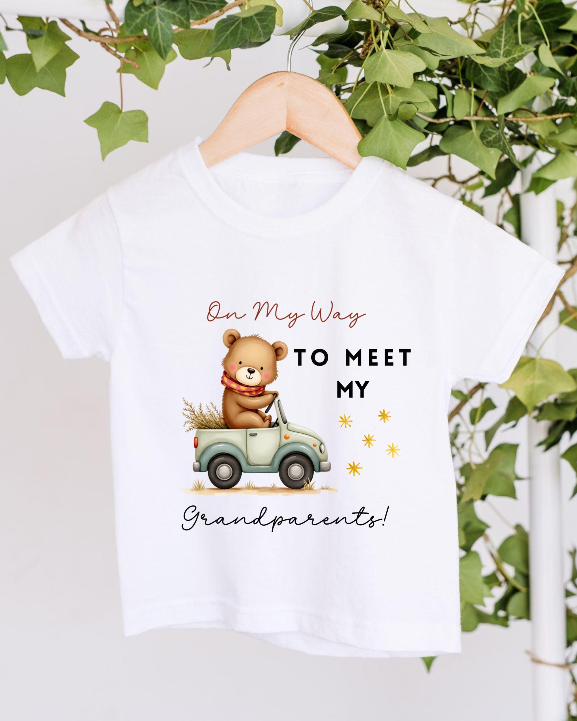 A white t-shirt with a cartoon image of a bear riding a car and text that says "On My Way to Meet My Grandparents!"
