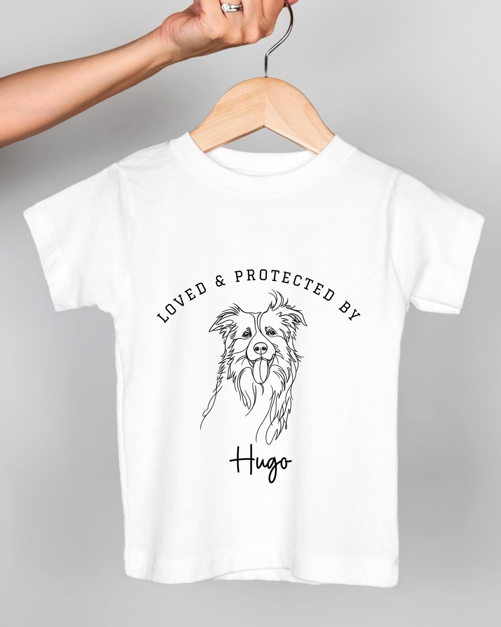 A white t-shirt with a graphic design of a dog's face and the text "LOVED & PROTECTED BY Hugo" printed on it.