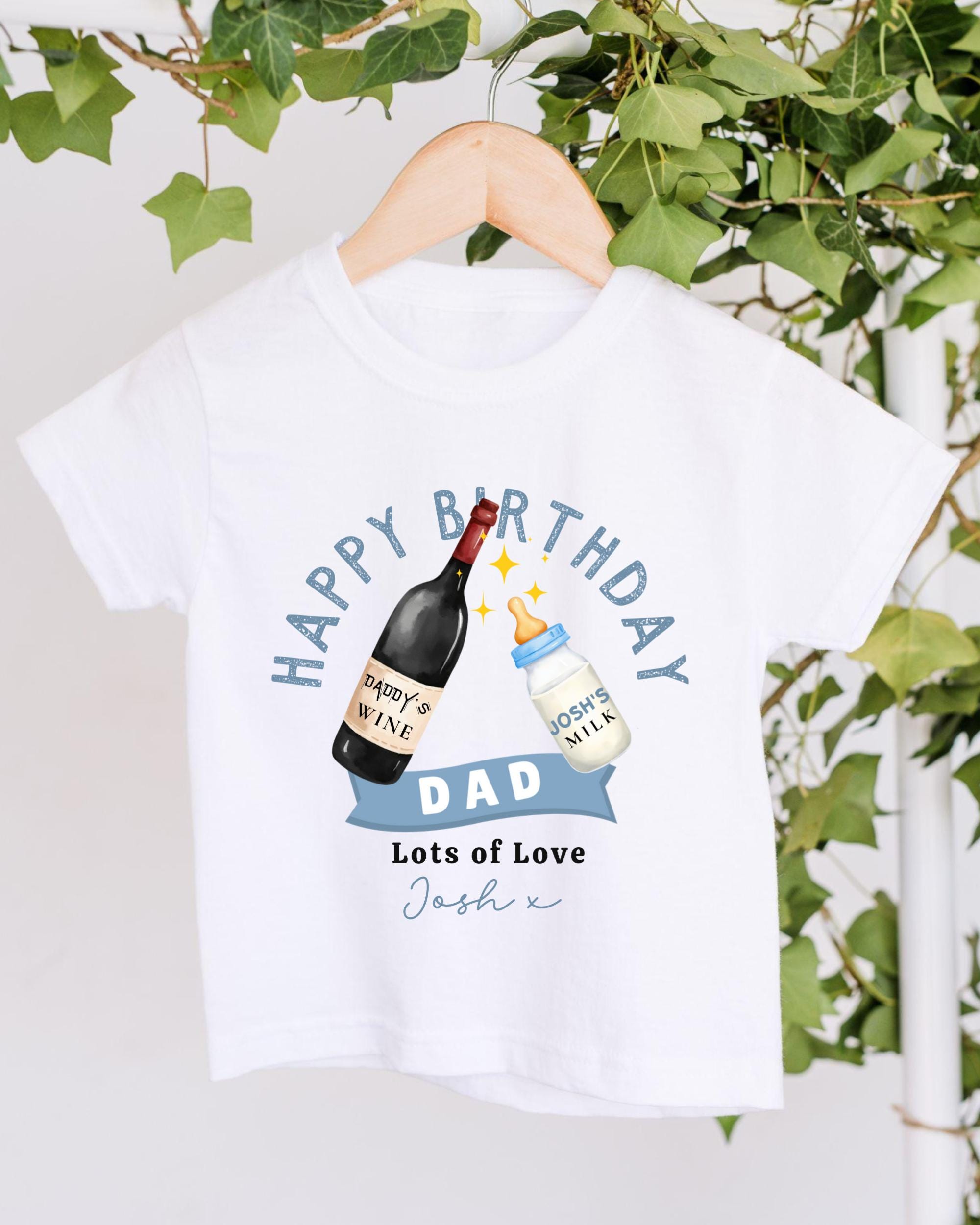 A white t-shirt with a graphic design featuring a bottle of wine and a baby bottle, along with the text "Happy Birthday Dad Lots of Love Josh".