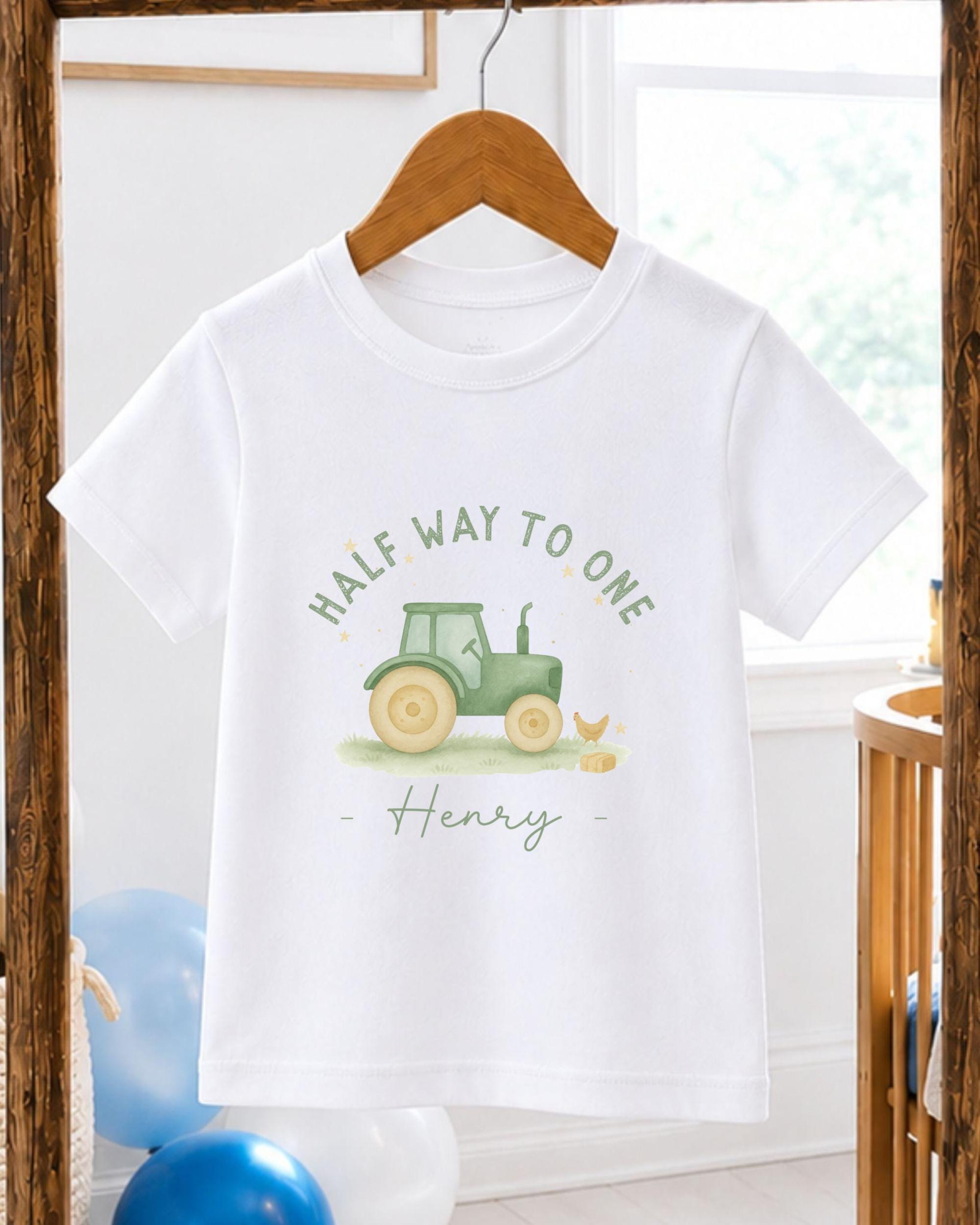 A white t-shirt with a graphic design of a tractor and a chicken, along with the text "Half Way to One Henry" printed on it.