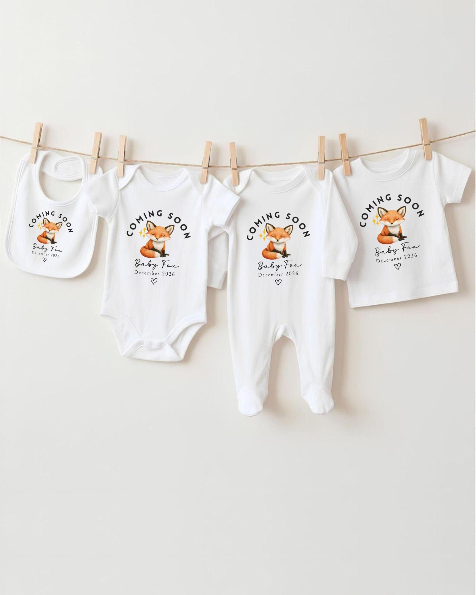 A row of white baby clothes with the text "Coming Soon Baby Fox December 2016" printed on them, along with a small image of a fox.