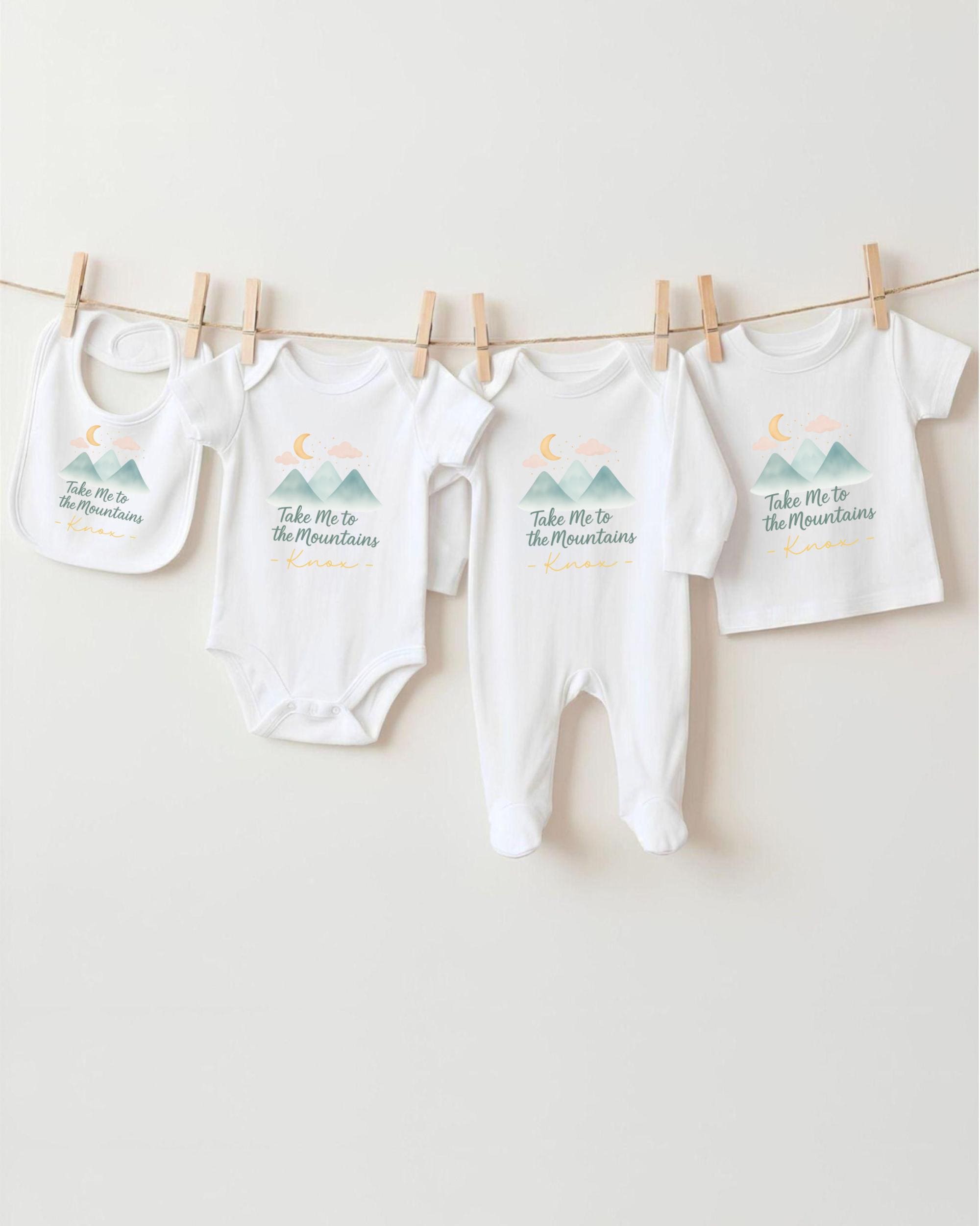 A row of four white baby clothes with mountain and moon designs hanging on a clothesline.