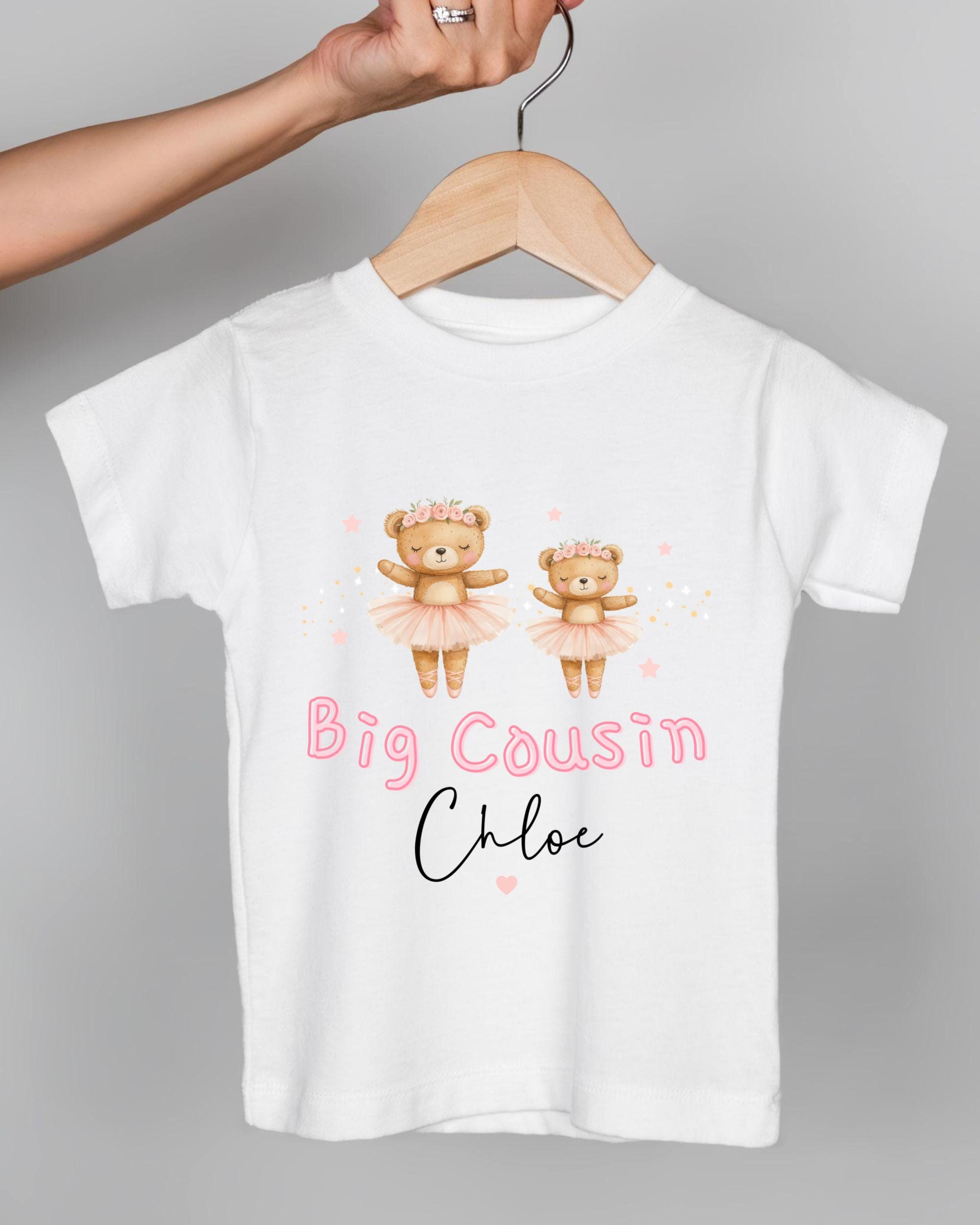 A white t-shirt with a design featuring two teddy bears in tutus and the text "Big Cousin Chloe" printed on it.