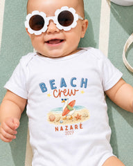 A smiling baby wearing a white onesie with a beach-themed design and sunglasses.