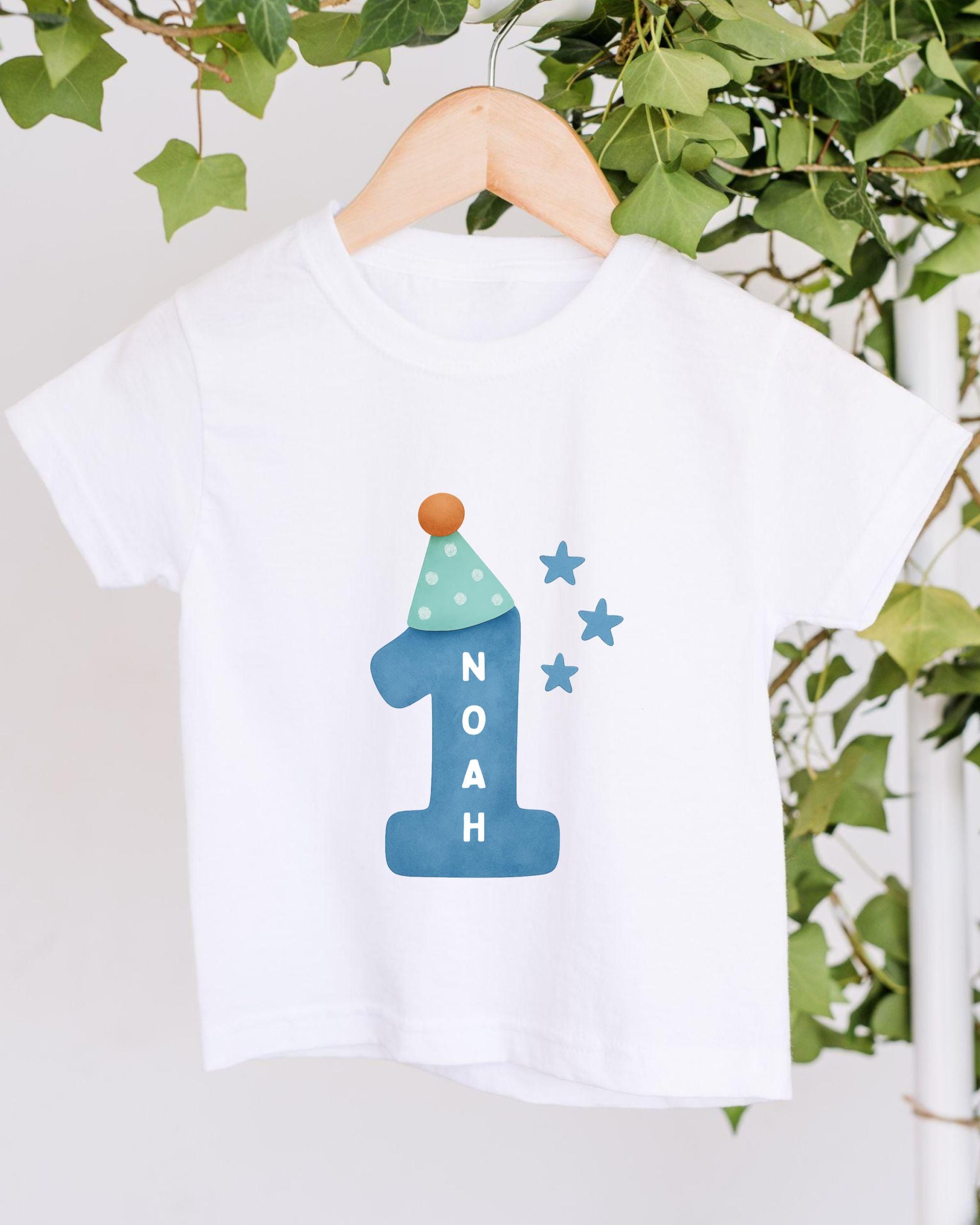 A white t-shirt with a blue number one and stars printed on it, hanging on a wooden hanger.