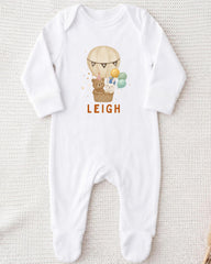 A white onesie with a printed image of a teddy bear and a hot air balloon, along with the name "LEIGH" printed on it.