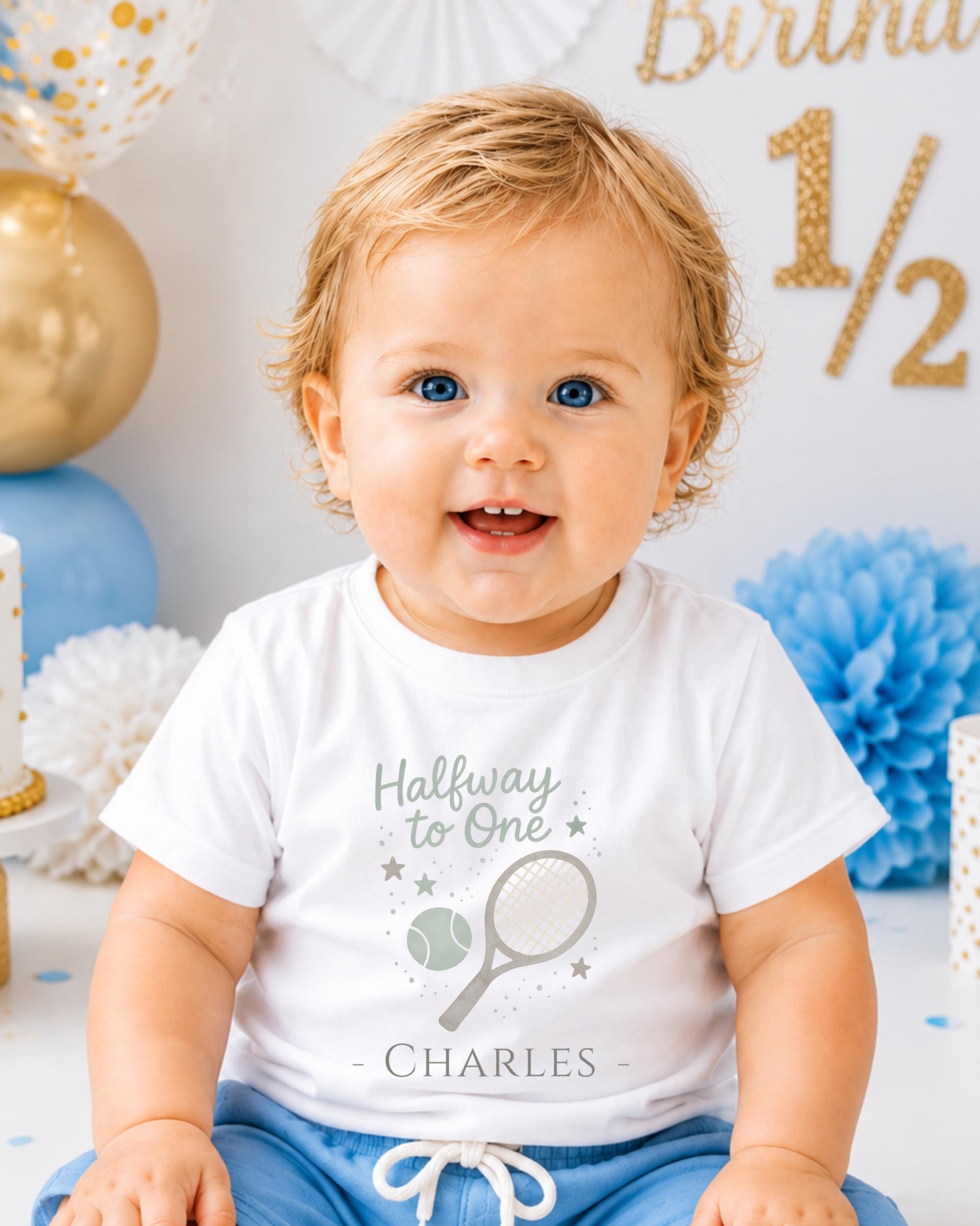 A smiling baby boy wearing a white t-shirt with a tennis racket and the text "Halfway to One" is sitting in front of a birthday party backdrop.