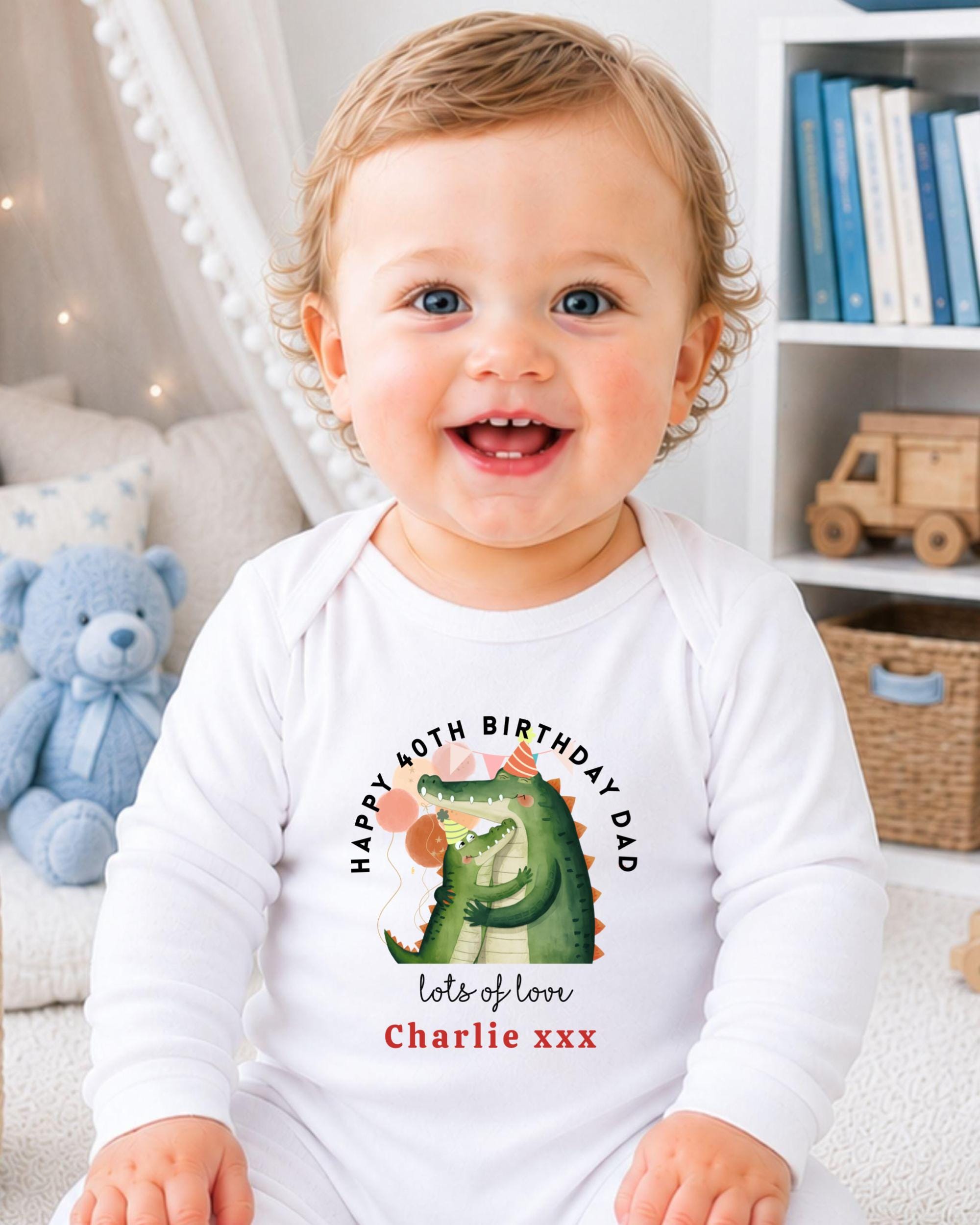 A smiling baby wearing a white onesie with a cartoon alligator and text that says "Happy 40th Birthday Dad lots of love Charlie xxx".