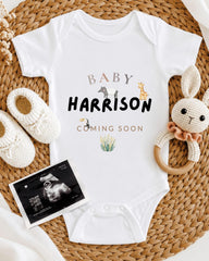 A baby's onesie with the name "Baby Harrison" printed on it, along with a crocheted rabbit toy and a baby bootie. There is also an announcement for an upcoming baby, which appears to be an ultrasound image.
