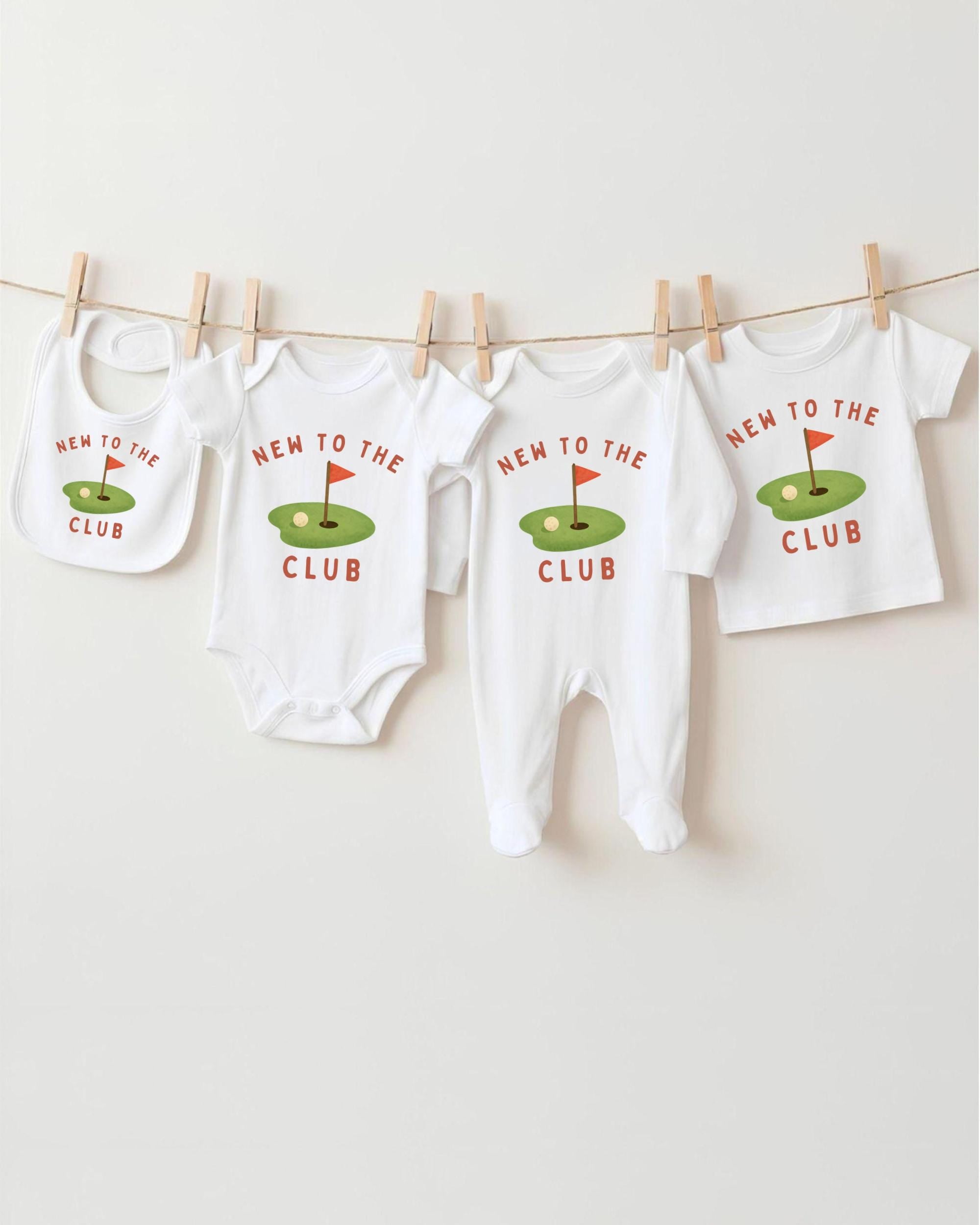 A row of four white baby clothes with the text "NEW TO THE CLUB" printed on them, hanging on a clothesline.