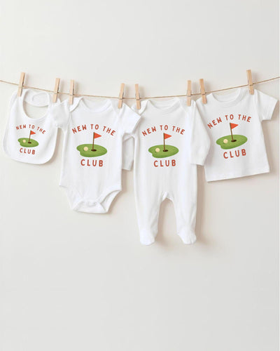 A row of four white baby clothes with the text "NEW TO THE CLUB" printed on them, hanging on a clothesline.