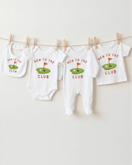 A row of four white baby clothes with the text "NEW TO THE CLUB" printed on them, hanging on a clothesline.