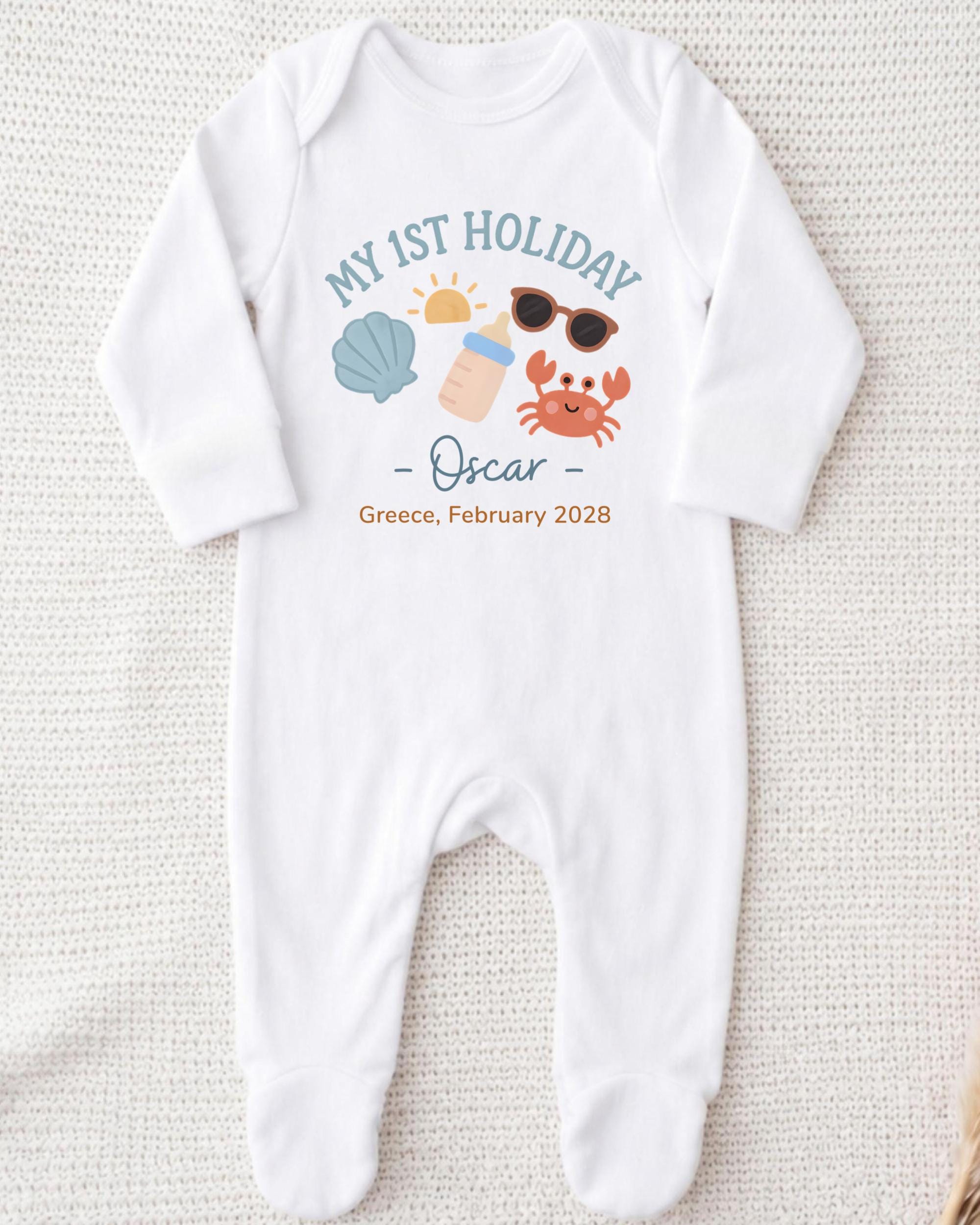 A white onesie with a graphic design on it, featuring icons of a sun, sunglasses, a shell, and a crab, along with the text "My 1st Holiday Oscar - Greece - February 2028".
