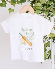 A white t-shirt with a graphic design and text printed on it, hanging on a wooden hanger.