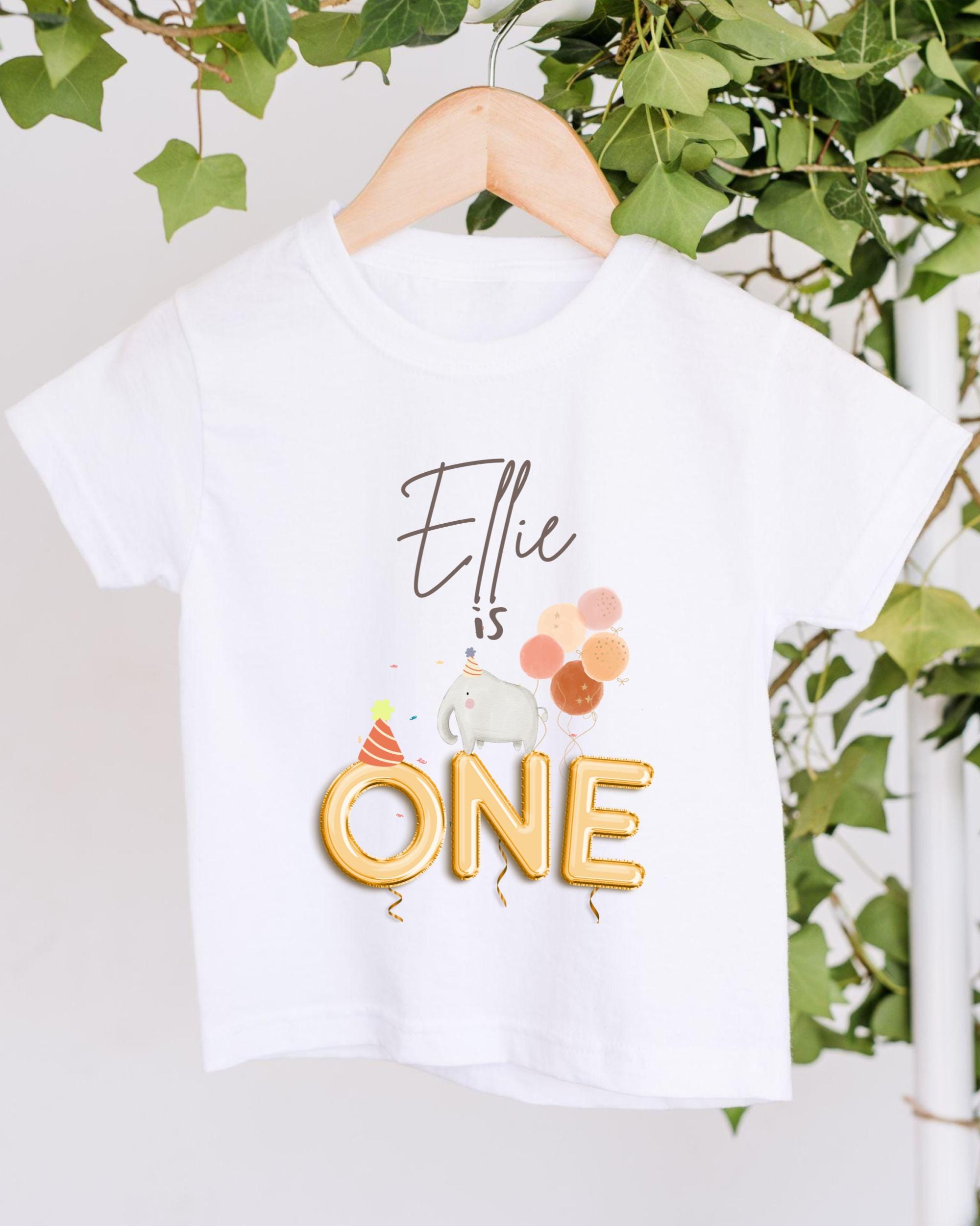 A white t-shirt with a personalized text and graphic design, hanging on a wooden hanger.