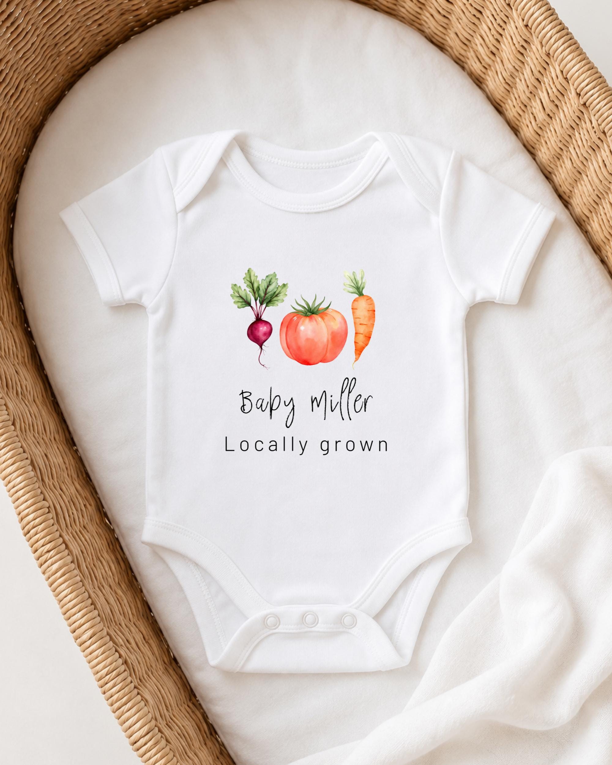 A white baby onesie with a graphic of a carrot, radish, and tomato, along with the text "Bappy Miller Locally grown".