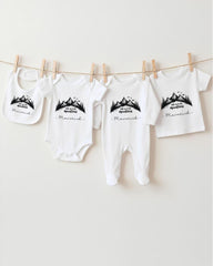 A collection of baby clothes, including onesies and pajamas, hanging on a clothesline.