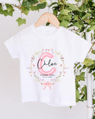 A white t-shirt with a floral design and the name "Chloe" printed on it, hanging on a wooden hanger.