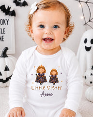 A smiling baby girl wearing a white onesie with a Halloween-themed design, including two princesses and the text "Little Sister Annie".