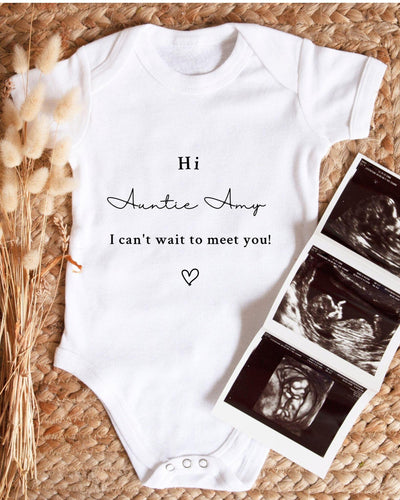 A white baby bodysuit with text and a heart symbol, placed next to a set of three black and white baby ultrasound images.