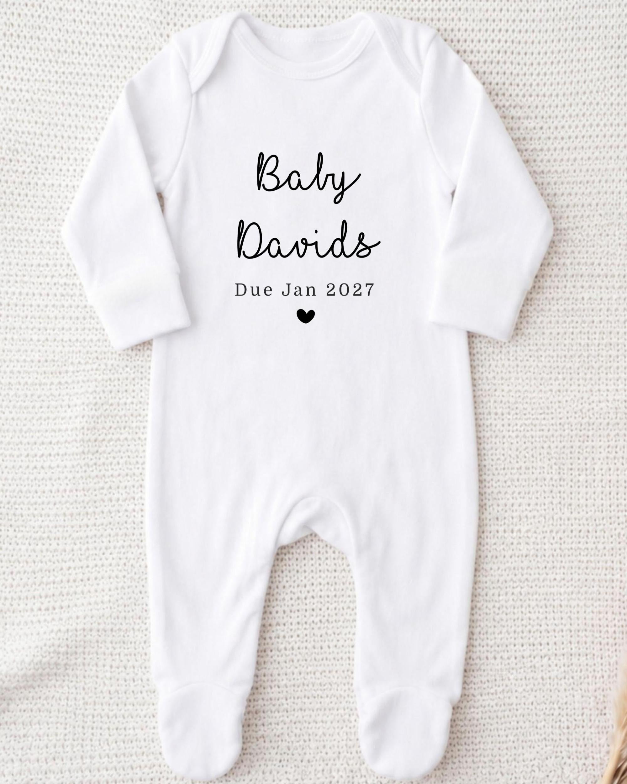 A white onesie with the text "Baby David's Due Jan 2027" printed on it.