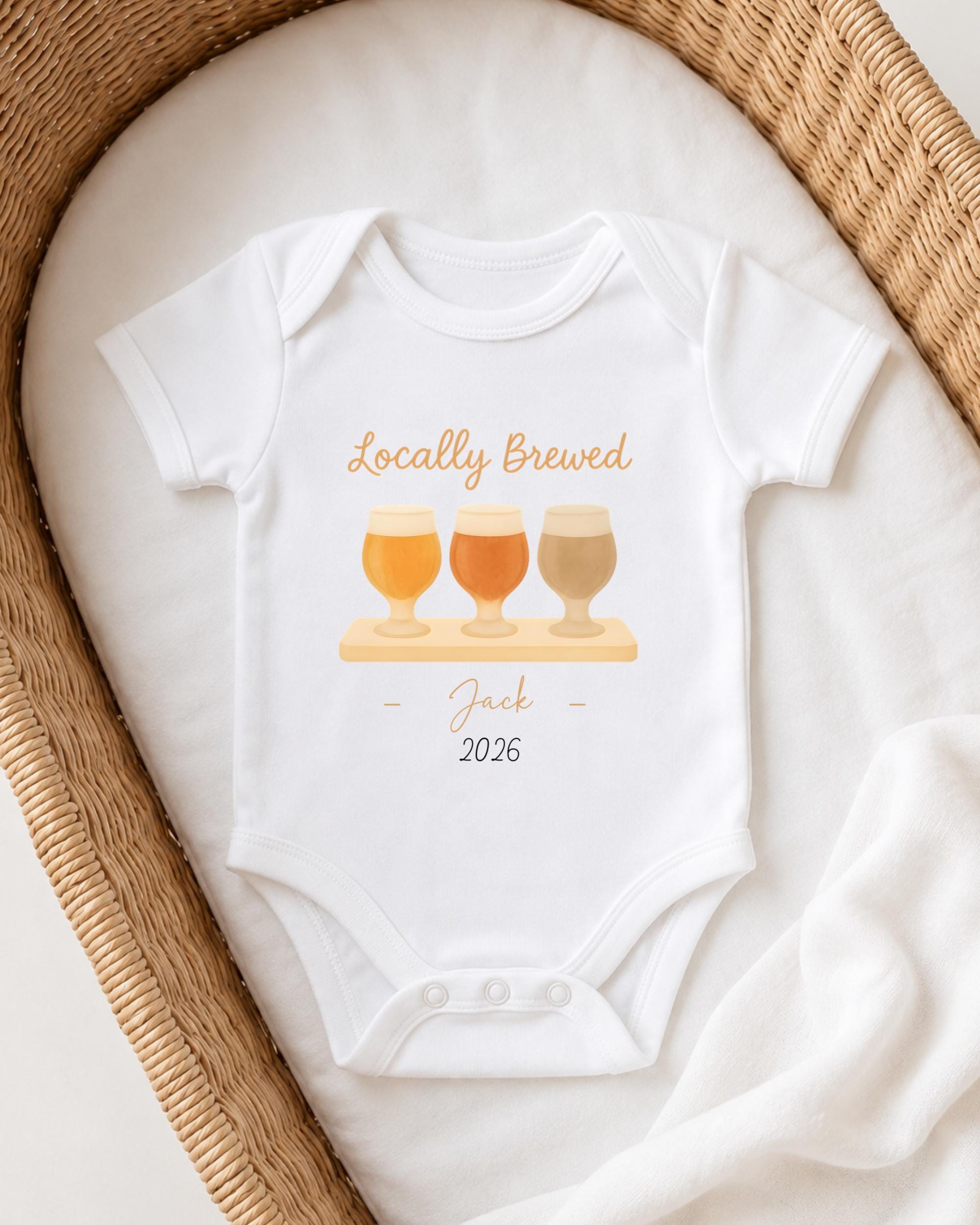 A white onesie with a graphic design of three beer glasses and the text "Locally Brewed Jack 2026" printed on it, placed on a white cloth.