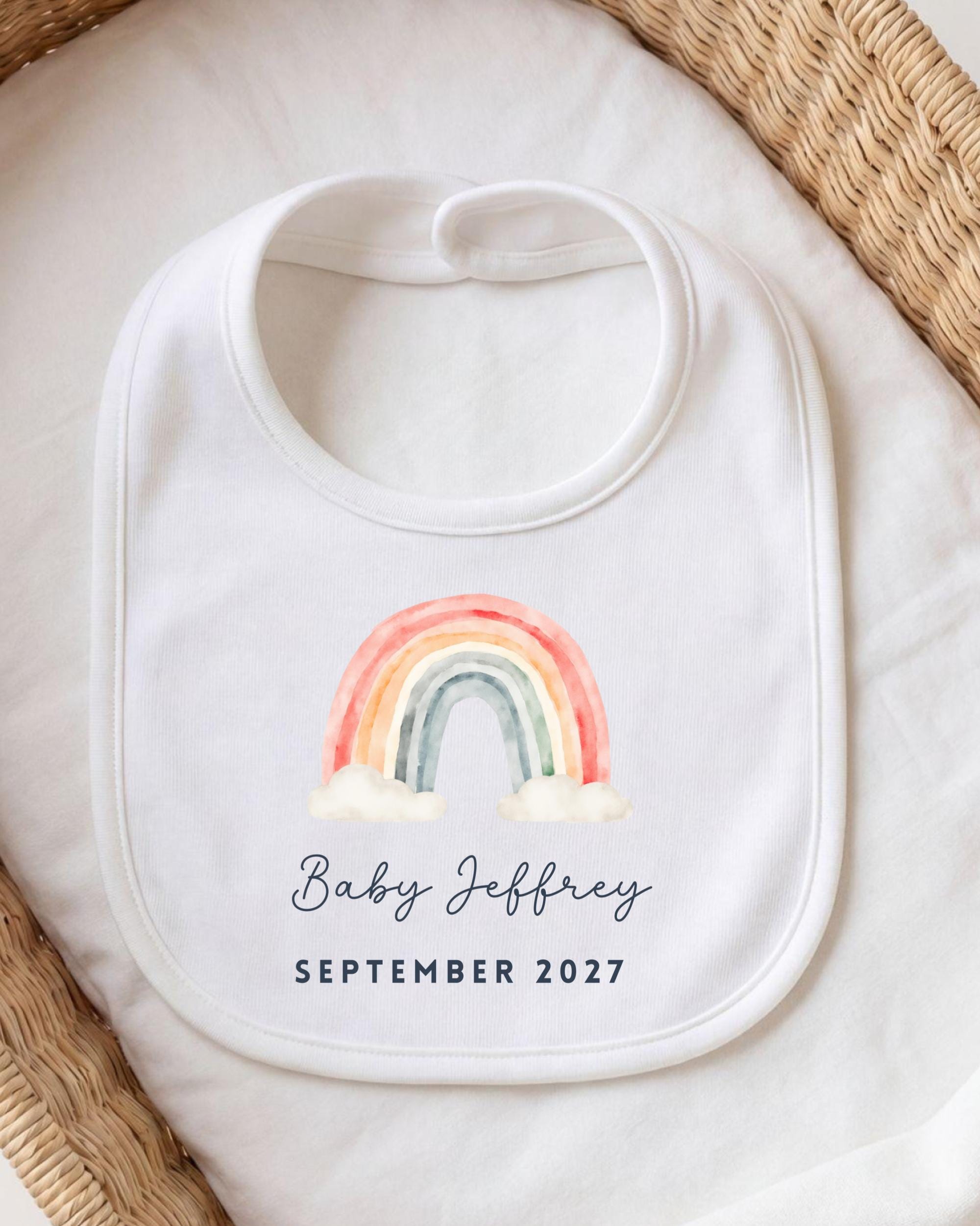 A white bib with a rainbow graphic and the text "Baby Jeffrey September 2027" printed on it.