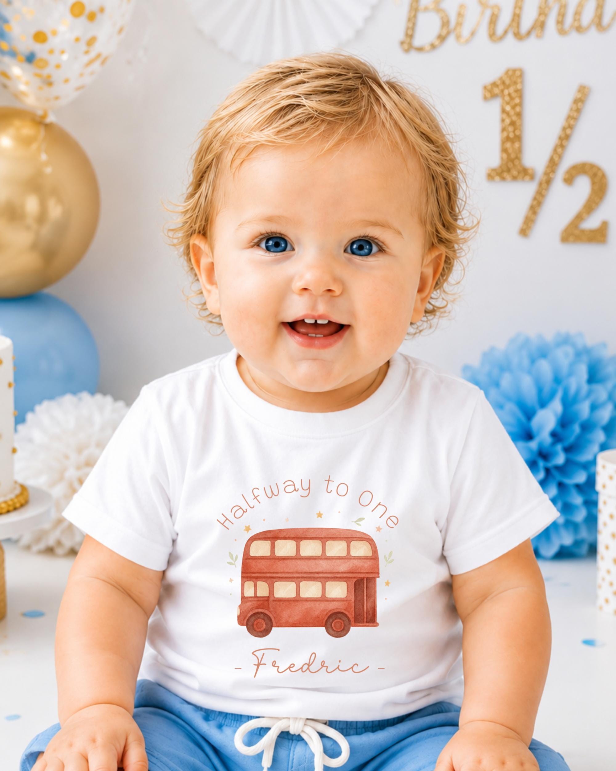 A smiling baby boy wearing a white t-shirt with a red double-decker bus graphic and the text "Halfway to one - Frederic" is sitting in front of a birthday party backdrop.