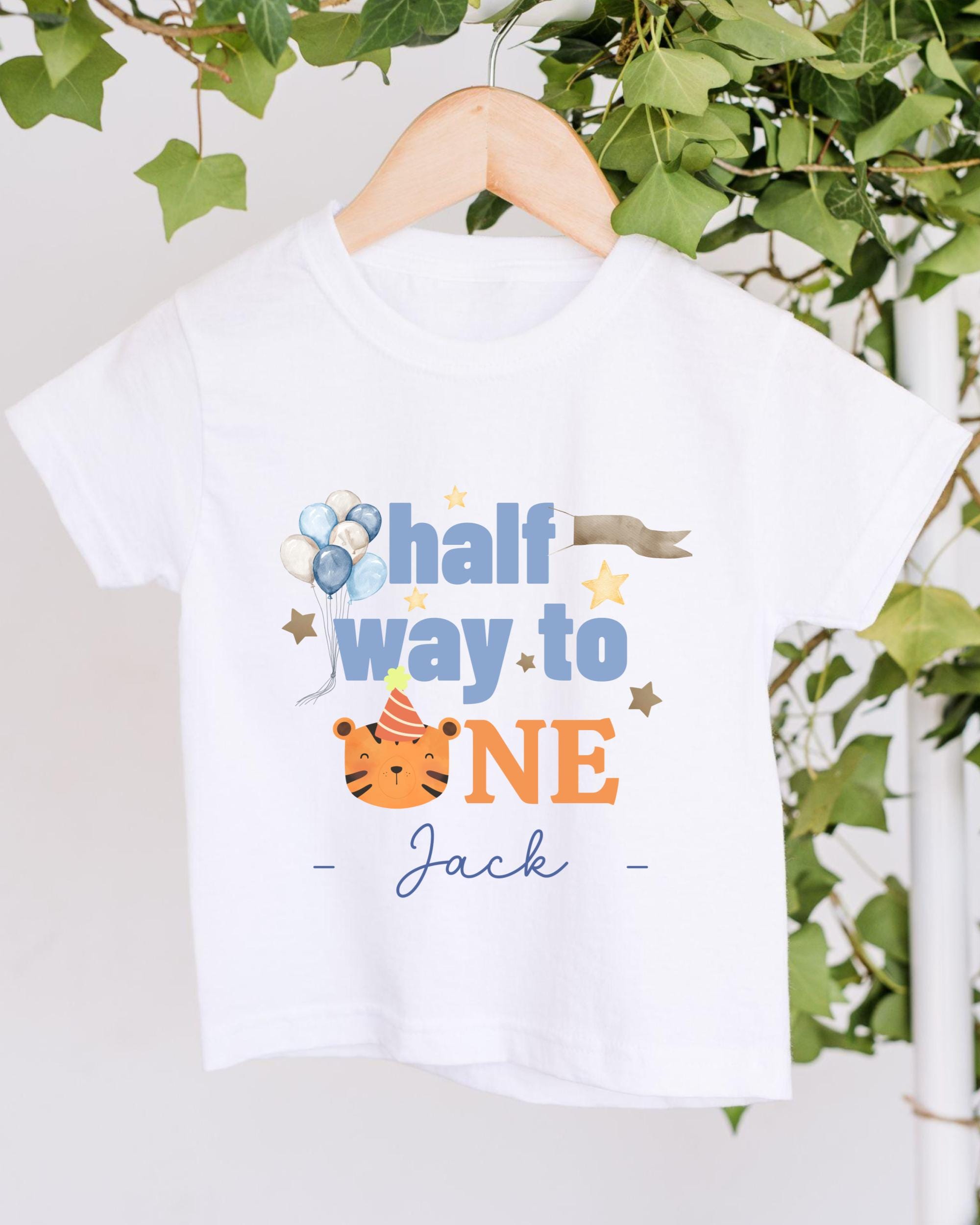 A white t-shirt with a printed design that says "half way to one" and features a tiger wearing a party hat.
