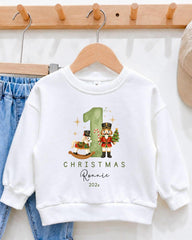 A white sweatshirt with a Christmas-themed design, featuring a nutcracker and a rocking horse, along with the text "CHRISTMAS Ronnie 2021".