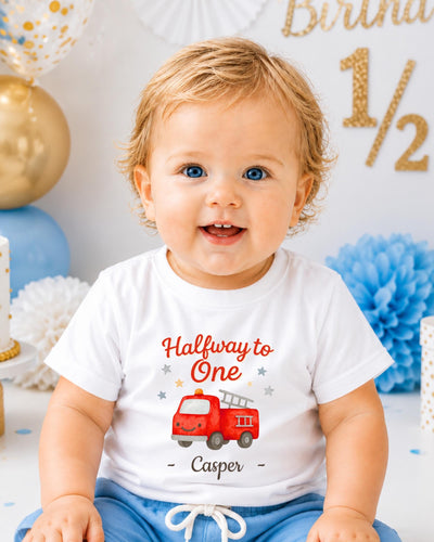 A smiling baby boy wearing a white t-shirt with a red fire truck graphic and the text "Halfway to One - Casper" printed on it.