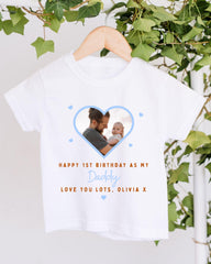 A white t-shirt with a photo of a man holding a baby inside a heart shape, along with the text "Happy 1st Birthday as my Daddy Love you lots, Olivia X".